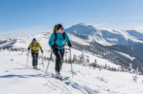 Dva skialpinisté stoupají na lyžích zasněženým svahem.