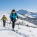 Dva skialpinisté stoupají na lyžích zasněženým svahem.